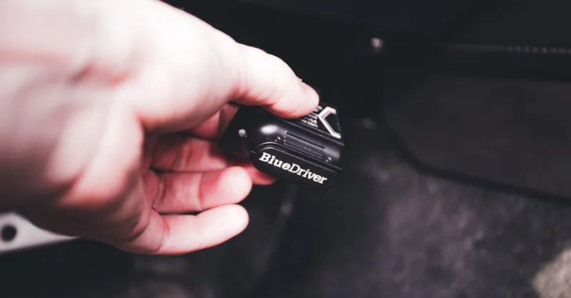Close-up of a hand connecting a BlueDriver diagnostic device in a vehicle. Ideal for automotive and technology themes.