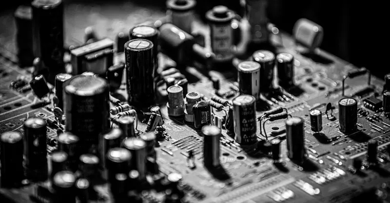 Grayscale close-up of electronic circuit board with capacitors and transistors.