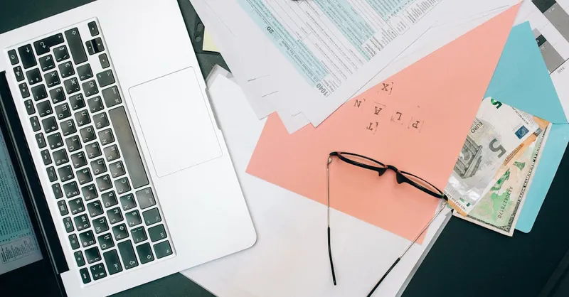 A tidy workspace featuring a laptop, documents, and eyeglasses for productivity.