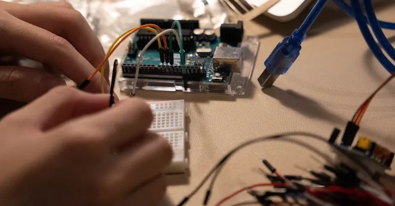 Close-up of hands assembling electronic components on a breadboard with wires.