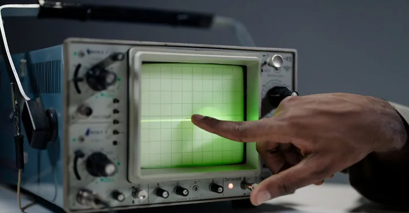 A hand pointing at the screen of a vintage oscilloscope indoors.