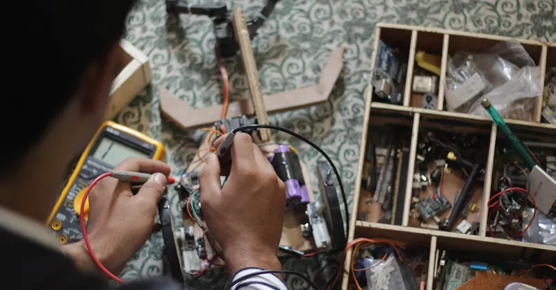 Man soldering electronic parts at a table filled with tools and equipment.