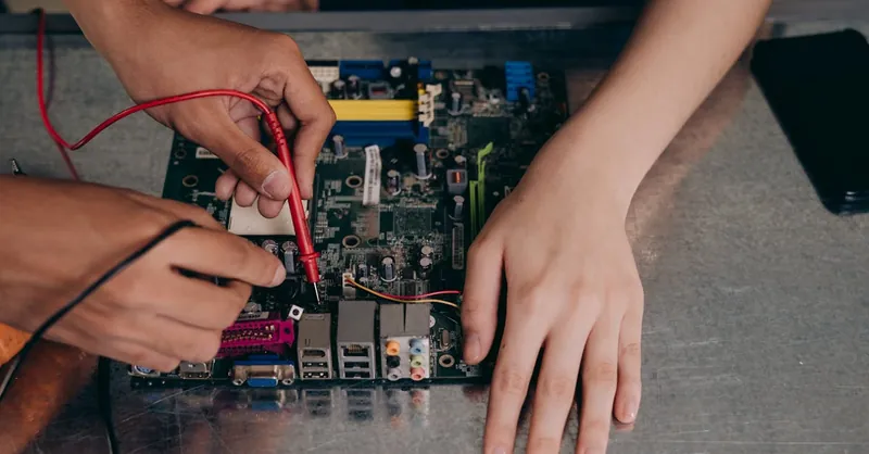 Hands working with electrical tester on motherboard, showcasing technical repair skills.