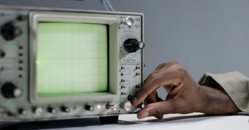 A person adjusts settings on a vintage oscilloscope in a studio environment.