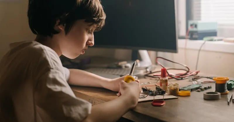 A young person soldering electronic components, showcasing DIY engineering and hobbyist skills indoors.