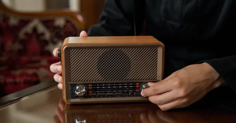 Person adjusting vintage wooden radio knob, close-up indoor shot.